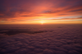 Hyper-realistic aerial view above clouds bathed in deep red and golden sunset light